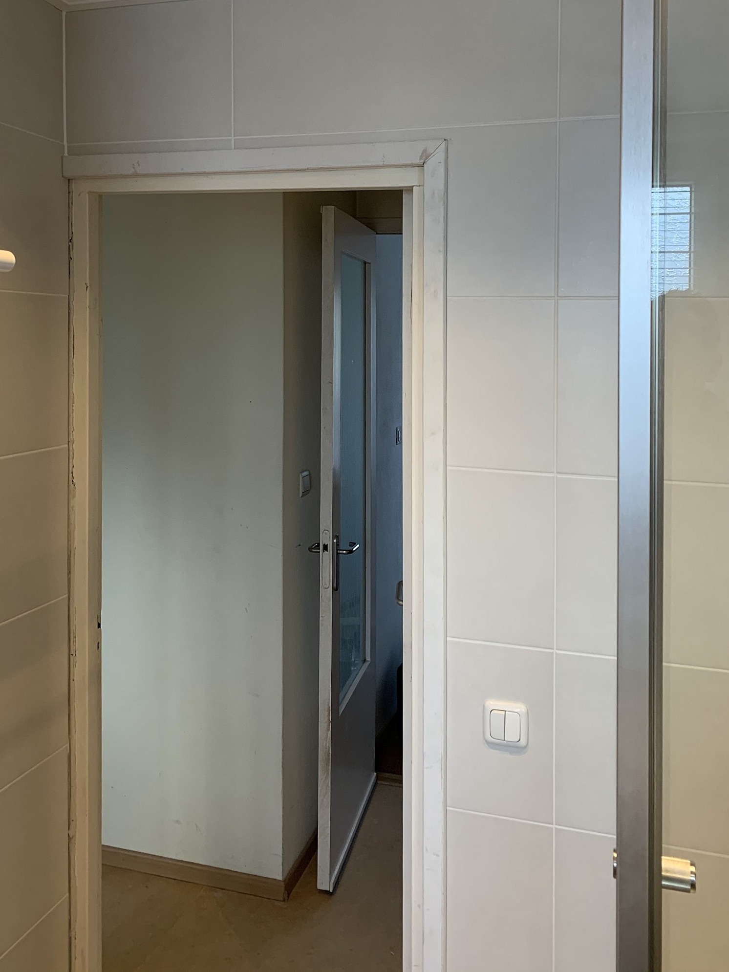 Opgeleverde badkamer met betegelde wand, deurkozijn en glazen douchewand
